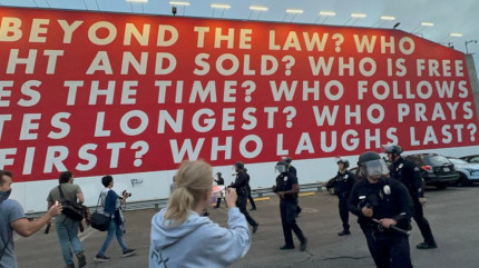 WHO IS 
BEYOND THE LAW? WHO IS BOUGHT AND SOLD? WHO IS FREE TO 
CHOOSE? WHO DOES TIME? WHO FOLLOWS ORDERS? WHO SALUTES 
LONGEST? WHO PRAYS LOUDEST? WHO DIES FIRST? WHO LAUGHS 
LAST? Barbara Kruger mural at the Temporary Contemporary 
behind an apparent confrontation between journalists 
and Law Enforcement in downtown LA a couple days ago