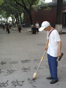 man writing Chinese characters on the sidewalk with a long wand, in Beihai Park